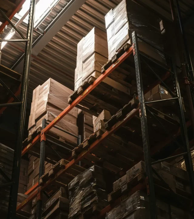 Interior view of a warehouse with stacked cardboard boxes on high shelves, showcasing storage and logistics.